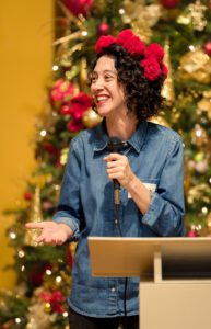 A woman stands smiling at a podium with a microphone.
