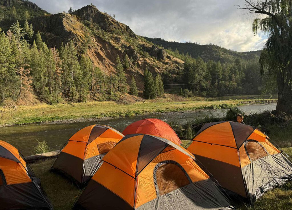 22-25b_Klamath-Camping-web Five orange tents are arranged in a campsite along the Klamath River
