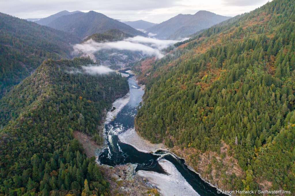 Klamath River flows between two mountain sides with cloudy sky in background.