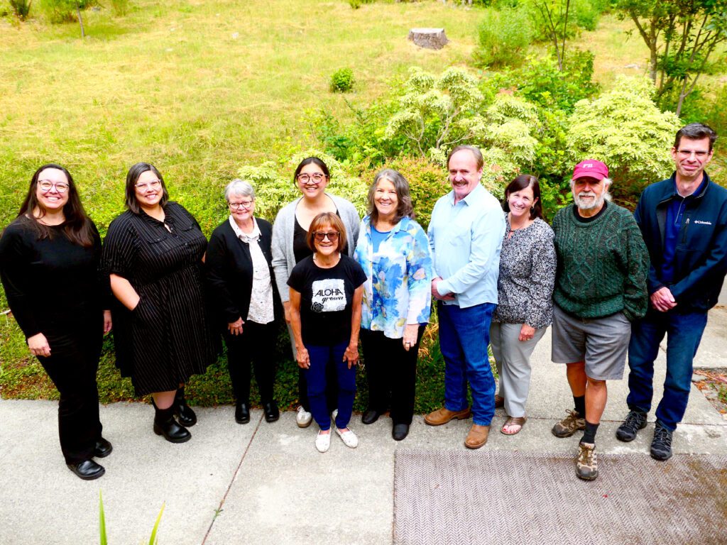 Ten people stand outside in front of a hill and smile up at the camera.