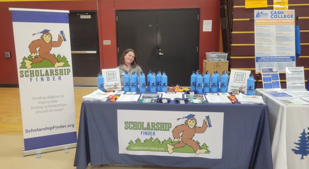 Young woman sits at table covered in Scholarship Finder gear.