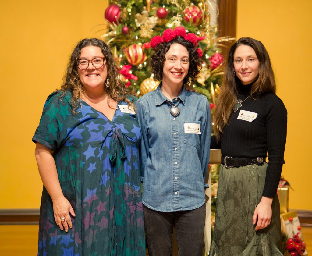 Three women pose in front of a Christmas tree.